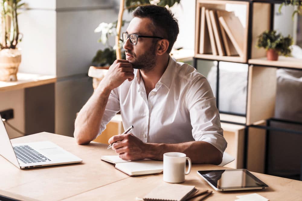 Thoughtful mature man holding pen and looking away while sitting | How To Identify, Research + Decide On Your Niche | how to find a niche market | finding a niche market