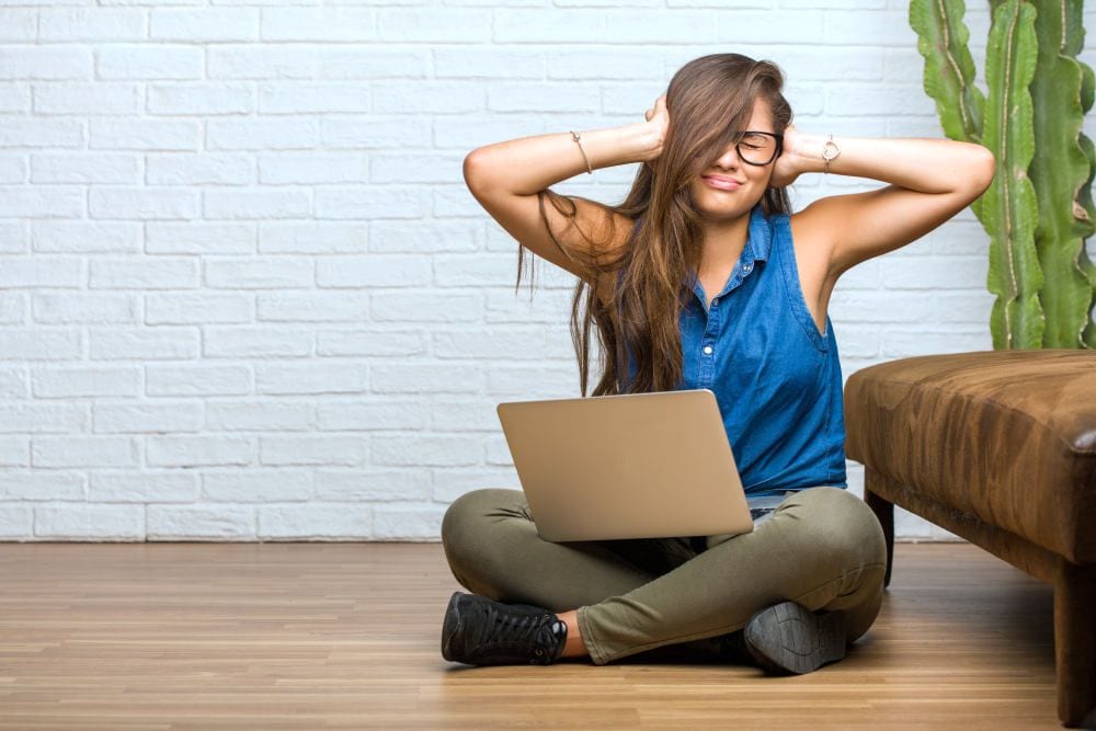 Portrait of young latin woman sitting on the floor covering ears | Distractions When Working From Home And How To Avoid Them | how to avoid distractions | distractions at work