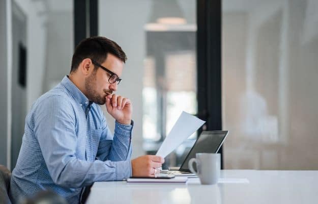 Thoughtful businessman in the office looking at and working with laptop and papers ss