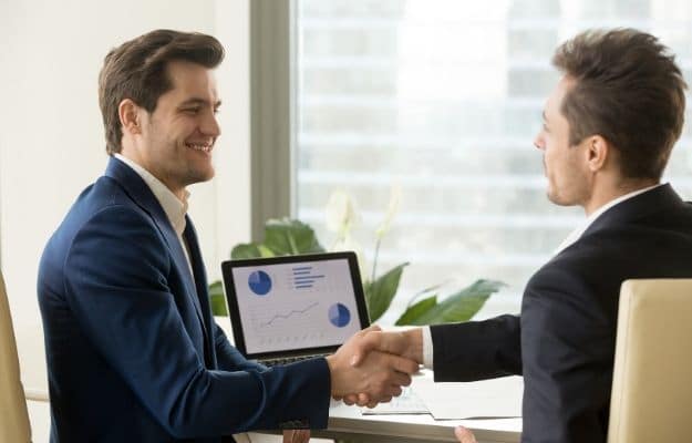 Two smiling businessmen handshaking sitting at desk with charts graphs ss