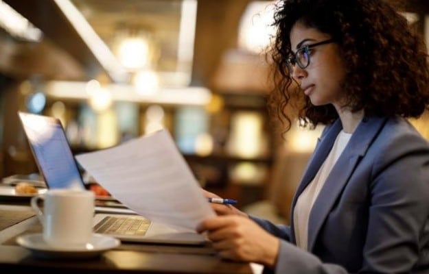 a business woman is watching the laptop and holding papers us