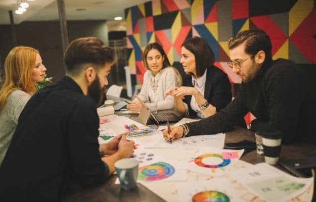 five people are working in a office with colorful wall ca