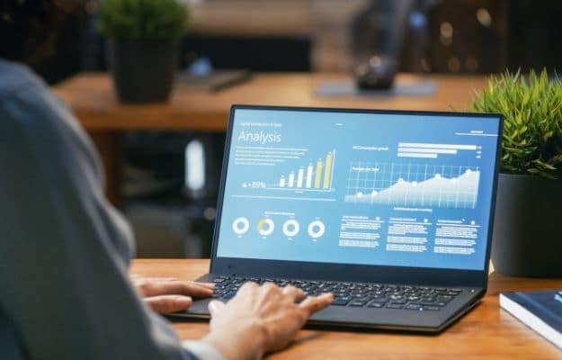 Female Analyst at Her Desk Works on a Laptop Showing Statistics ss