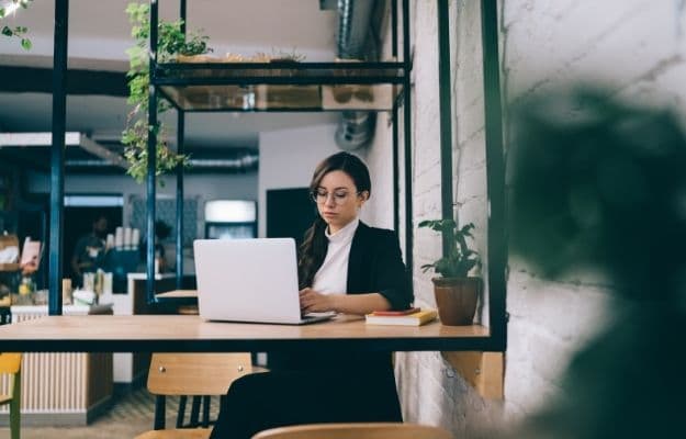 Modern focused confident business woman in glasses and black suit using laptop while sitting at the coffee shop ss