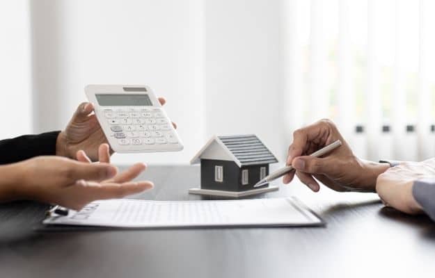 one person is holding the calculator one person is holding the pen and the model of the house